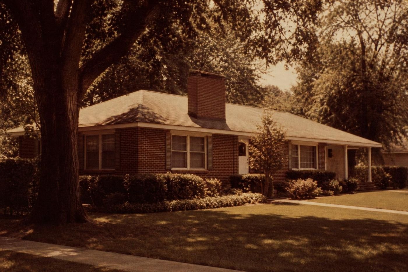 Brick ranch house with a wide chimney and mature trees